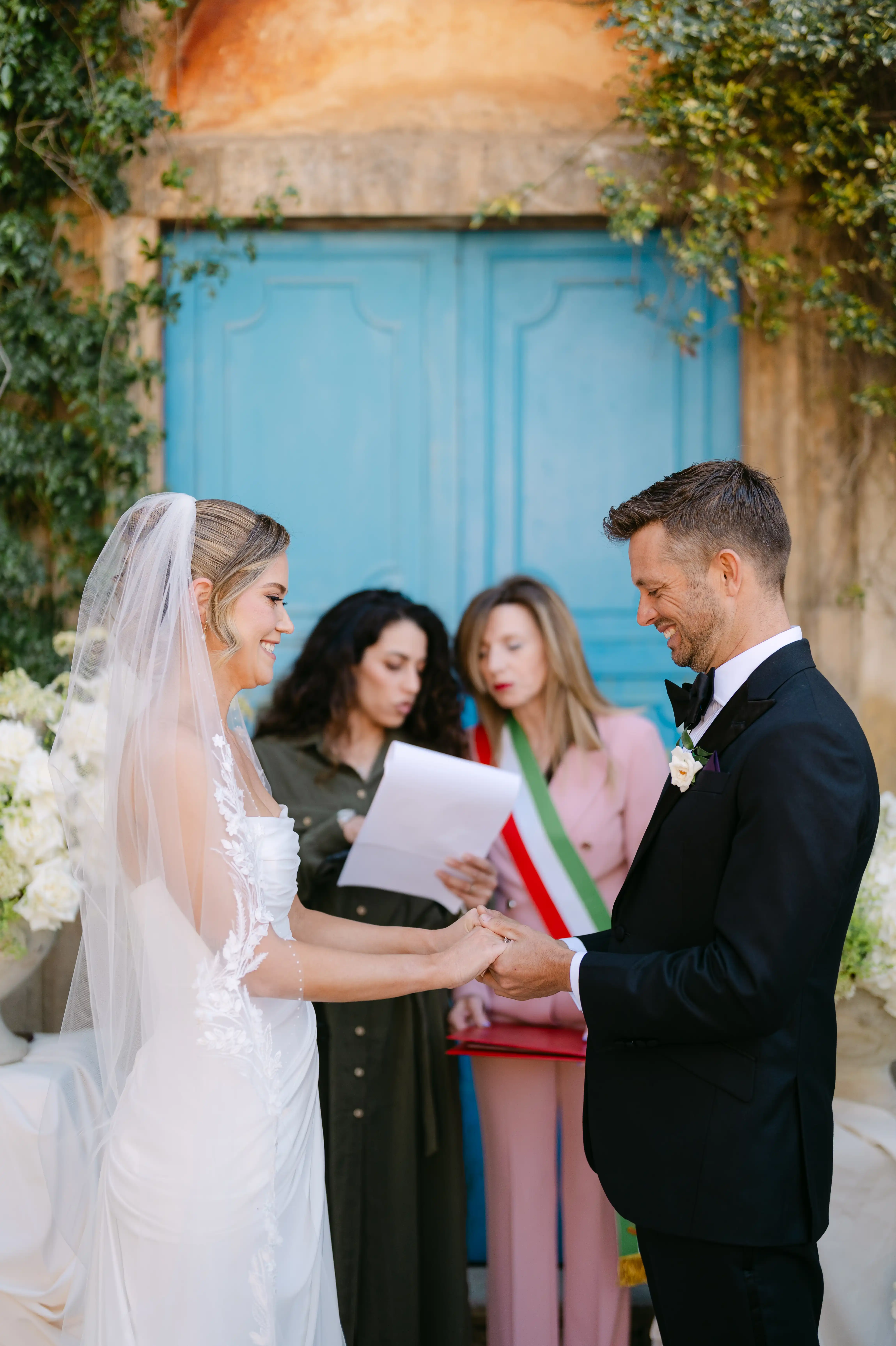 Bride and groom exchanging vows in front of a blue rustic doorway during a romantic Sicilian wedding ceremony.